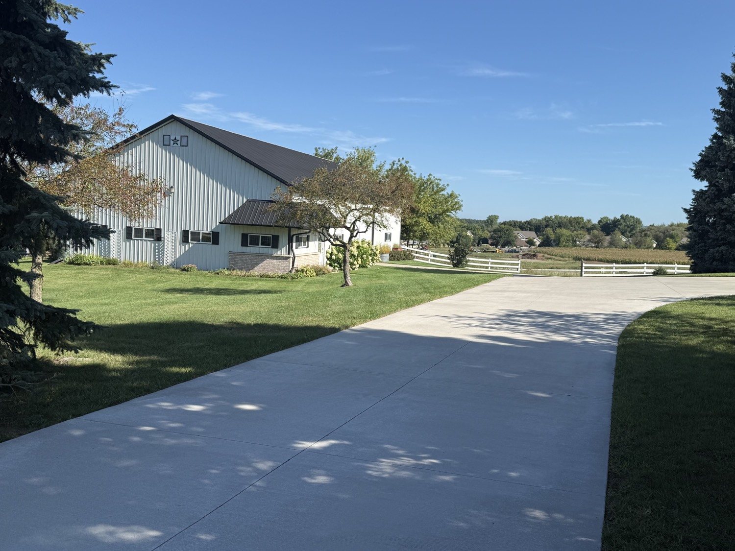 White pole barn with a freshly mowed lawn along a long concrete driveway